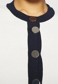 Knit cardigan featuring a white body with a navy trim, four metallic buttons down the front, and a ribbed collar.