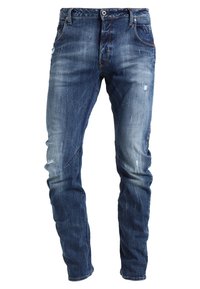 Tummansiniset farkut, joissa on slim fit -leikkaus, vaaleaa kulumista, pieniä kulutustietoja ja perinteinen viiden taskun tyyli.