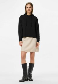 Svart hooded sweatshirt med snoddar, kombinerad med en ljusbeige knälång kjol. Modellen bär svarta läderknähöga stövlar med detaljer.