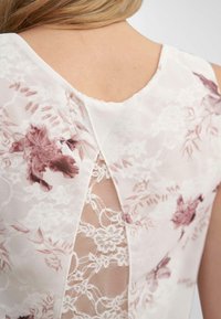 Robe à motifs floraux en rose clair avec un insert en dentelle texturée dans le dos et un décolleté en V, présentant un tissu doux et transparent.