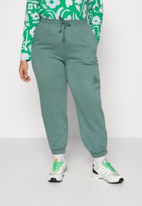 Mintgröna sweatpants med elastisk midja, sidofickor och ribbade muddar; har en präglad Adidas-logotyp på vänster lår.