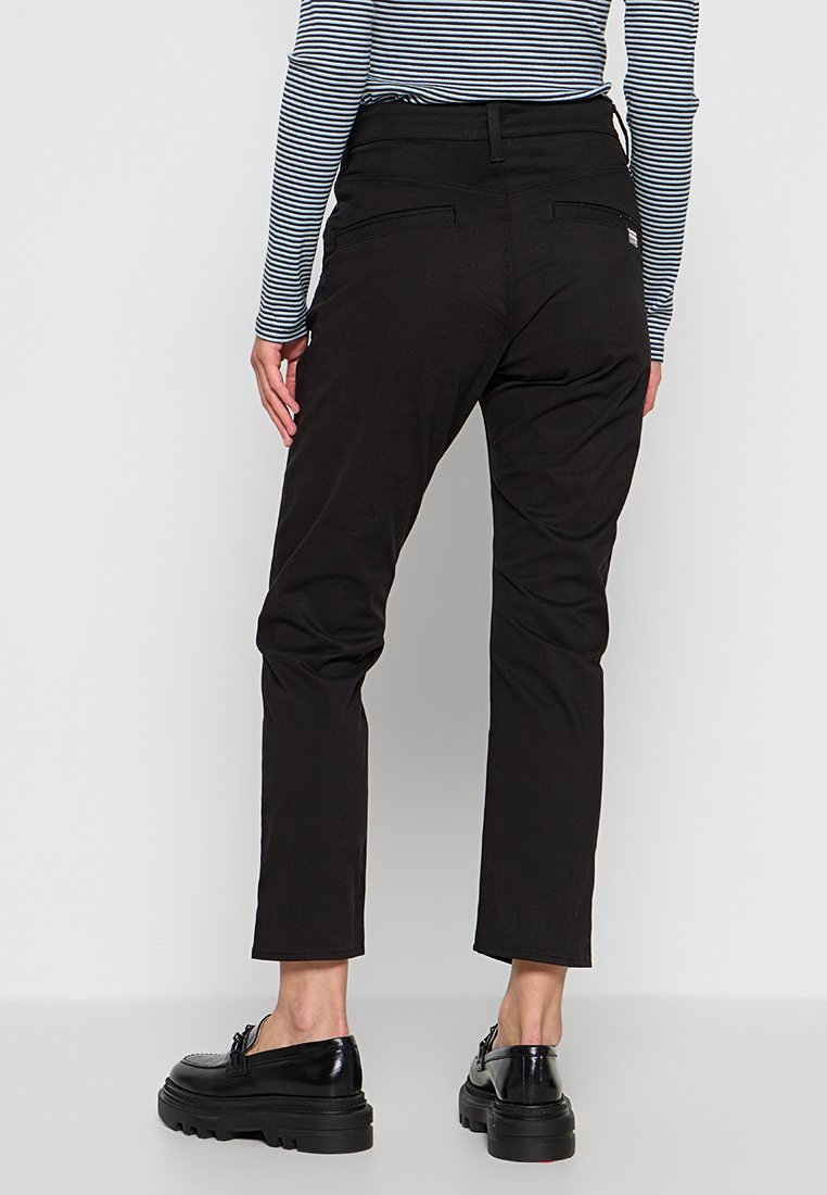 Pantalons noirs fuselés avec une texture lisse, dotés d'une taille mi-haute et de deux poches arrière. Portés avec un haut rayé noir et blanc.