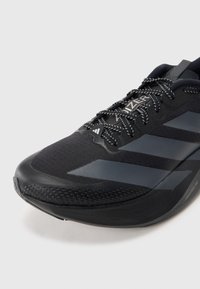 Chaussure de course noire avec une tige synthétique texturée. Présente un design élégant, des accents réfléchissants, et une semelle en caoutchouc rembourrée pour une bonne adhérence.