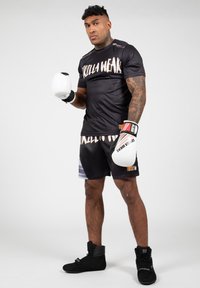 Zwarte sportieve T-shirt met korte mouwen met de tekst "GORILLA WEAR", gecombineerd met zwarte shorts en bokshandschoenen. Draag het met zwarte hoge sneakers.