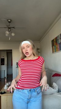 Rotes und weiß gestreiftes ärmelloses Oberteil mit rundem Ausschnitt, kombiniert mit hoch taillierten hellblauen Jeans, in einem häuslichen Umfeld.