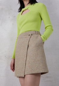 Haut côtelé vert fluo avec une découpe en trou de serrure, associé à une mini-jupe en tweed beige ornée de flecks colorés et d'un unique bouton.