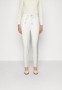 Witte taps toelopende broek met een elastische tailleband en trekkoord, voorzien van zijzakken en een gladde textuur. Gemaakt met lichtgekleurde schoenen.