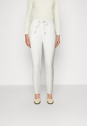 Witte taps toelopende broek met een elastische tailleband en trekkoord, voorzien van zijzakken en een gladde textuur. Gemaakt met lichtgekleurde schoenen.