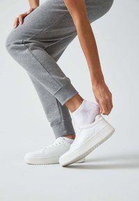 Weiße Sneakers aus glattem Leder mit runder Zehenpartie und dicker Gummisohle, kombiniert mit grauen Jogginghosen und weißen Socken. 