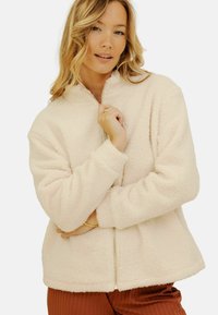 Veste en polaire crème avec fermeture éclair, col montant et texture douce. Dotée de manches longues et d'une coupe décontractée.