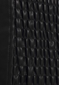 Schwarzes strukturiertes Leder mit einem gesteppter Muster und gepolsterten Abschnitten. Glatt und feinkörnig, wodurch eine taktile Oberfläche entsteht.