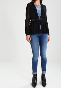 Svart stickad kofta med ett texturerat mönster, bälte i midjan; kombinerad med blå skinny jeans och spetsiga svarta ankelboots.