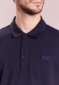 Námořnické polo tričko z texturované látky s tříknoflíkovou légou, klasickým límečkem a modrým vyšívaným logem na hrudi.