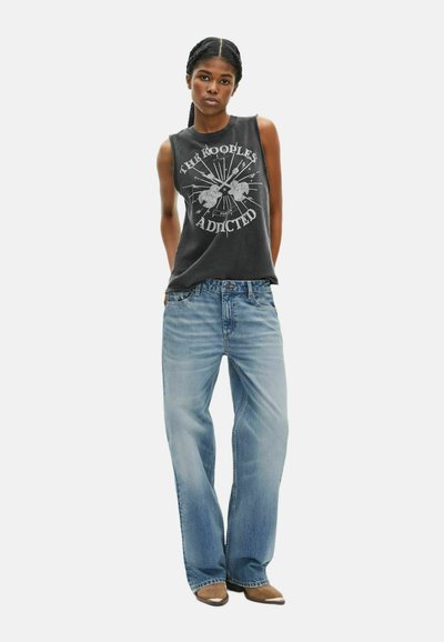 Zwart mouwloos graphic tanktop met een zilveren print, gecombineerd met lichtblauwe wijde jeans en bruine haklaarzen.