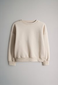 Sweat-shirt beige oversize à col rond avec poignets et ourlet côtelés, présenté à plat sur un fond gris clair.