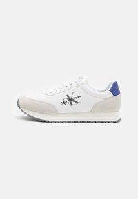 Zapatilla blanca con parte delantera de ante gris, trabilla trasera azul y logo de Calvin Klein Jeans en gris. Cierre de cordones planos, suela de goma y interior acolchado.