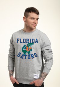 Šedá bavlněná mikina s nápisem "Florida Gators" a grafikou krokodýla v zelené a oranžové barvě. Žebrované manžety a lem. Štítek v levém dolním rohu.
