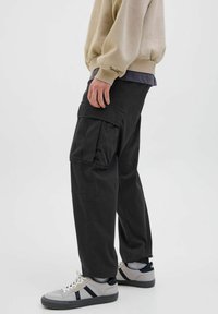 Schwarze Cargo-Hosen mit mehreren Seitentaschen, hergestellt aus strapazierfähigem Stoff. Kombiniert mit hellgrauen Sneakern mit schwarzen Akzenten.