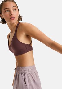 Sujeción deportiva inalámbrico en un tono malva profundo, con tejido suave y elástico, tirantes anchos y escote en forma de u, diseñado para prendas deportivas.