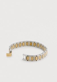 Sudraba un zelta rokassprādze ar taisnstūrveida savienotājiem; tā apvieno teksturētas un gludas virsmas, un vienā galā ir aizdare ar logotipu.