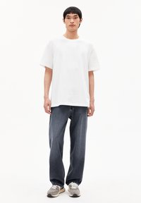 T-shirt en coton blanc avec une coupe décontractée, associée à un jean large bleu foncé. Des baskets grises avec des accents beiges complètent la tenue.