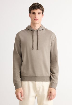 Hoodie en coton marron avec un cordon de serrage et des poignets côtelés. Présente un logo sur la poitrine et une coupe décontractée, assorti à un pantalon clair.