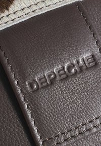 Hnědá kůže s embosovaným brandingem "DEPECHE", s texturovaným povrchem a kontrastním prošíváním podél okraje.