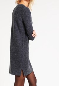 Dark gray knit sweater dress with a relaxed fit, featuring long sleeves and a slightly frayed hem. Side slit adds subtle detail.