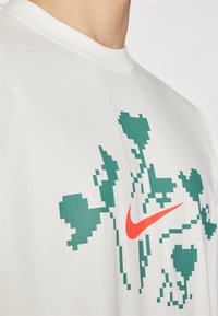 Camiseta de algodón blanca con un diseño de corazón verde pixelado y un destacado logotipo de Nike en color naranja en la parte frontal.