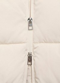 Beige pufferjack met verticale gestikte padding, met een dubbele ritssluiting en metalen hardware voor duurzaamheid. Zachte textuur.