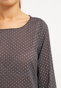 Blusa grigia con collo rotondo, maniche lunghe e motivo a rombi bianchi. Tessuto leggero con una trama leggermente trasparente.