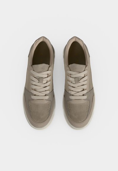 Ζευγάρι μπεζ casual sneakers με κορδόνια, από πάνω, σε απλό λευκό φόντο.
