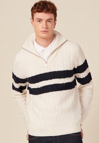 Cremfarbener, kabelgestrickter Pullover mit marineblauen horizontalen Streifen, hohem Kragen und Reißverschluss. Mit strukturiertem Muster und geripptem Saum.