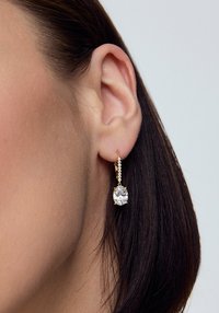 Złote kolczyki w stylu drop z kwadratowym kryształem otoczonym mniejszymi kryształami, z teksturowanym wzorem łańcuszka zawieszonym poniżej.