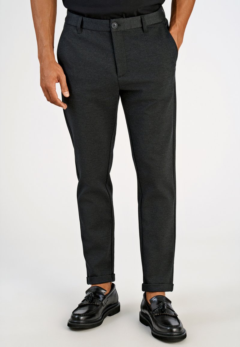 Meeste tumedat halli toonis tekstuurse kangaga püksid, millel on nööpkinnitused, küljetaskud ning kitsas lõige rullitud säärega. Sobitatud mustade kingadega.