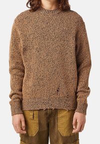 Maglione marrone a texture con collo rotondo, vestibilità ampia e polsini e orlo a coste. Presenta bordi sfilacciati e macchie scure sparse.