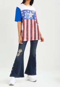 T-shirt con paillettes rosse, bianche e blu con pattern a stelle e strisce; abbinato a jeans in denim sfilacciati a vita alta e sneakers bianche.