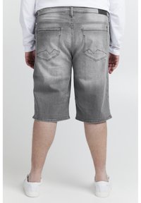 Graue Jeansshorts mit geradem Schnitt, ausgestattet mit Gesäßtaschen mit kantiger Naht und umgeschlagenen Säumen, getragen mit weißen Sneakers.