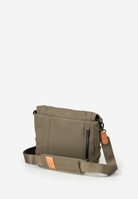 Olive green crossbody bag with adjustable strap, front zipper pocket, and tan leather zipper pull tab against white background.