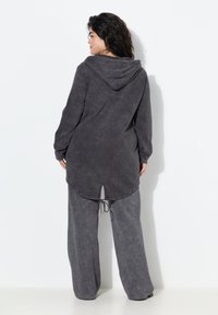 Sudadera gris con bolsillo canguro y cordón, combinada con pantalones de pierna ancha a juego. Tejido suave y texturizado con un corte relajado.