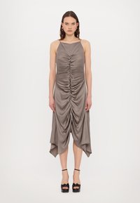Gray satin dress with ruched detailing and asymmetrical hem, featuring thin straps and a close fit, paired with black platform heels.
