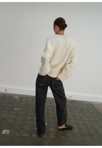 Suéter crema de gran tamaño con puños acanalados, combinado con jeans oscuros de tiro alto. Superficie texturizada, corte suelto y calzado negro sencillo.