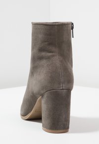 Šedá nubuková kotníková bota s kulatou špičkou, robustním podpatkem a uzavřenou zadní částí. Disponuje bočním zipem a hladkým povrchem.