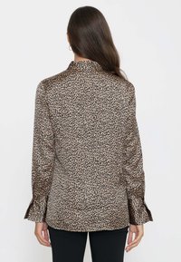 Blusa a stampa leopardata nei toni marrone e nero, con colletto classico e maniche lunghe con polsini abbottonati, realizzata in un tessuto liscio e lucido.
