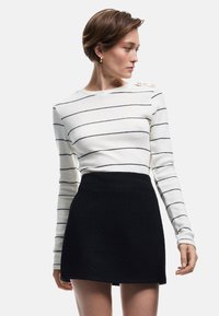 Gestreepte lange mouw top in wit en zwart, met schouderknopen; gecombineerd met een gestructureerde zwarte minirok.
