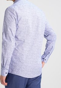 Long-sleeve shirt in light blue with a small white floral pattern, button cuffs, and a tailored fit. Cotton material with smooth texture.