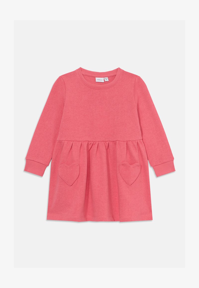 Rožinė megztinė su ilgomis rankovėmis, apvaliu iškirpimu ir surinkta juosmeniu. Priekyje yra širdelės formos kišenės.