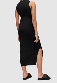 Robe noire moulante sans manches avec une fente latérale. Texture lisse et longueur jusqu'aux genoux. Associée à des sandales noires à enfiler.