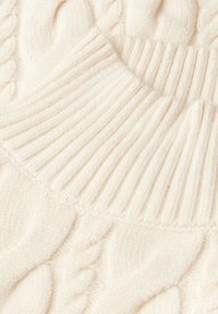 Sweter z warkoczem w miękkim kremowym kolorze, z prążkowanym kołnierzem i teksturowanym wzorem. Materiał wydaje się puszysty i ciepły, z przytulnym wykończeniem.