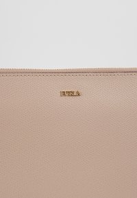 Světle růžová peněženka z texturované kůže se zlatým zipem a malým zlatým logem "FURLA" umístěným uprostřed při horním okraji.